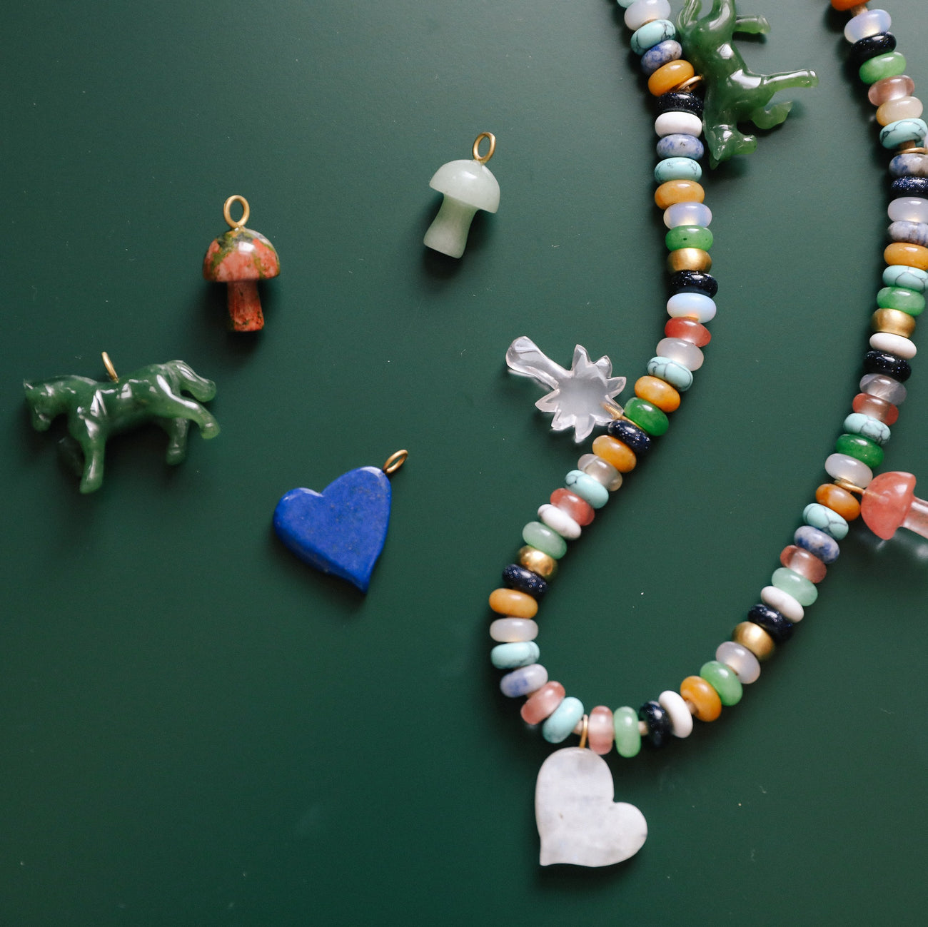 assorted stone charms and styled necklace sitting on green counter
