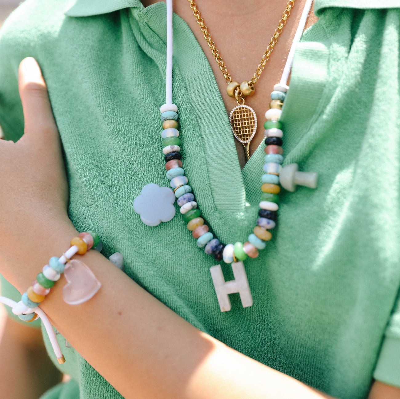 woman in green shirt wearing gold tennis racquet charmed necklace and assorted beaded necklace on a string